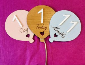 Baby age balloons in pink, wood varnish, blue showing ages 1 day, 1 today and 11 months.